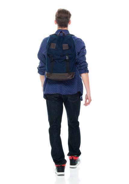 Caucasian boys university student walking in front of white background wearing backpack and holding bag Rear view of aged 16-17 years old with brown hair caucasian boys university student walking in front of white background wearing backpack who is showing cool attitude and holding bag ass boy stock pictures, royalty-free photos & images