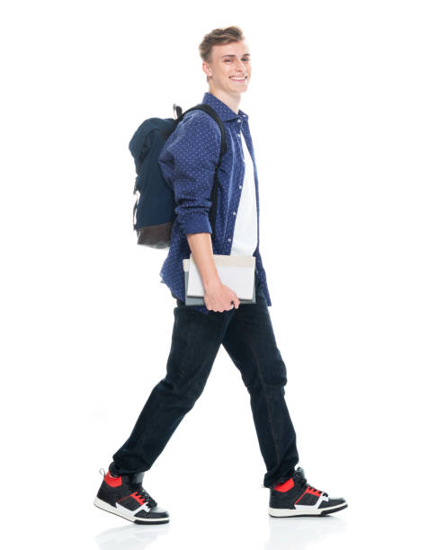 istock Boys high school student walking in front of white background wearing backpack and holding book 1211433134