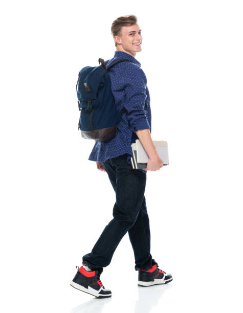 istock Caucasian boys high school student walking in front of white background wearing backpack and holding book 1211433171