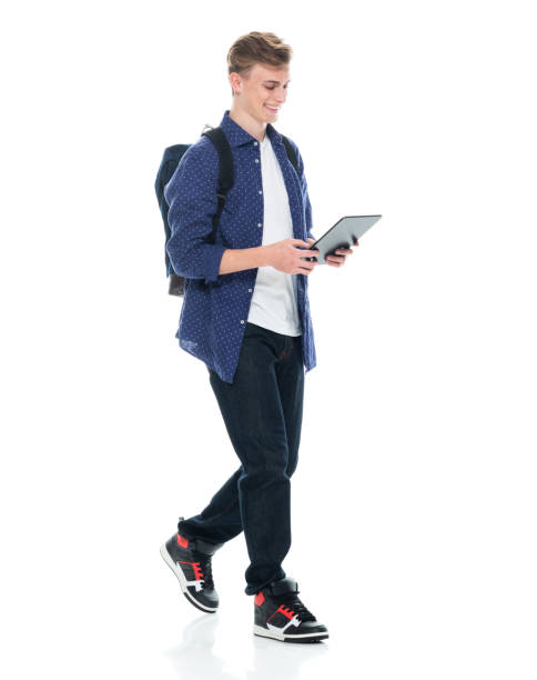 boys student walking in front of white background wearing backpack and holding textbook and using digital tablet - adult education full length book imagens e fotografias de stock