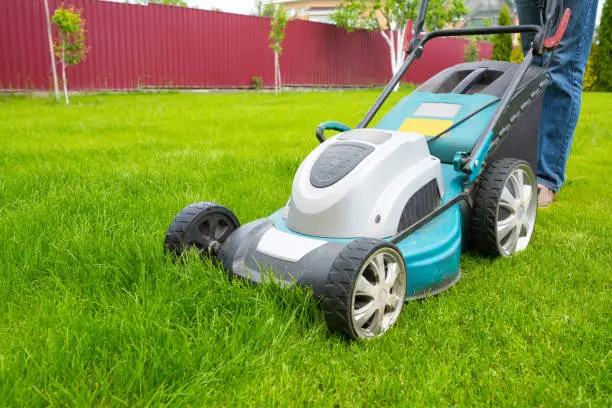 Photo of A lawn mover is cutting green grass, the gardener is working with a lawn mower, a close-up, the yard of a private house.
