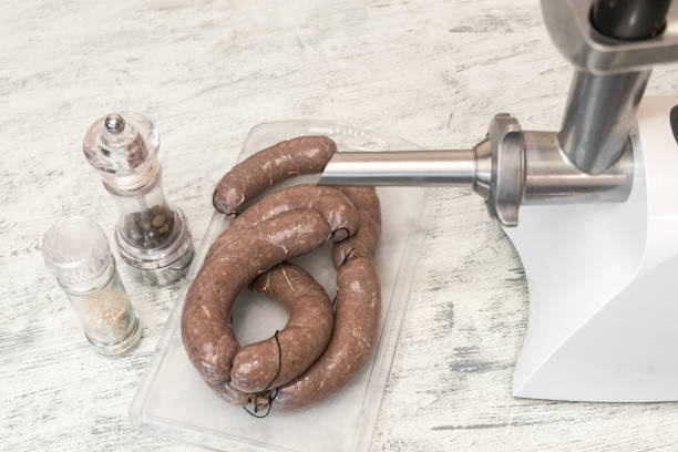 raw fresh homemade beef sausages in a natural shell on a wooden table close up. meat grinder for cooking minced meat and jars of spices. fast and nutritious food for picnics and barbecues - meat grinder ground beef meat imagens e fotografias de stock