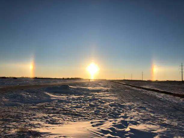 A sun dog in the distance, snow and a railway track frame the shot. The sun dog is a member of the family of halos, caused by the refraction of sunlight by ice crystals in the atmosphere.