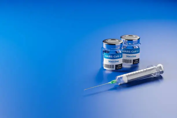 Vaccination against the new Corona Virus SARS-CoV-2: Two glass containers with 10 doses each and a syringe in front.