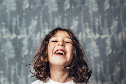 portrait of a happy little girl laughing on a blue background, happy childhood and lifestyle concept, copy space for text