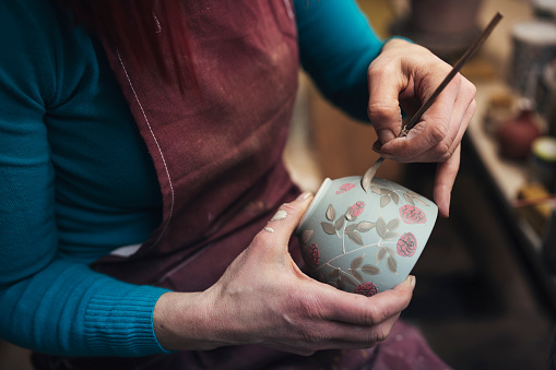 Unrecognisable female potter decorating  a clay pot in her workshop.