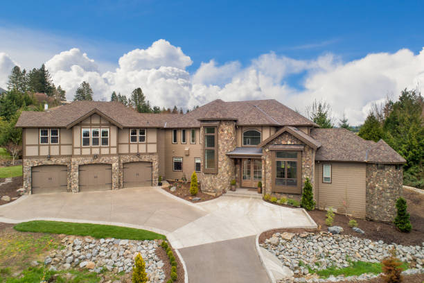 Beautiful large luxury home exterior on bright sunny day with blue sky. Features three car garage, turret, and elegant design