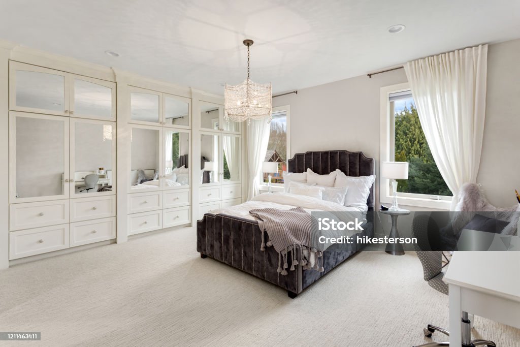 master bedroom in new luxury home with large windows, chandelier, carpet, and elegant decor. Master bedroom in luxury home Bedroom Stock Photo