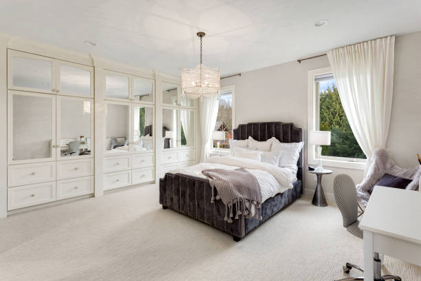 master bedroom in new luxury home with large windows, chandelier, carpet, and elegant decor. Master bedroom in luxury home owners bedroom photos stock pictures, royalty-free photos & images