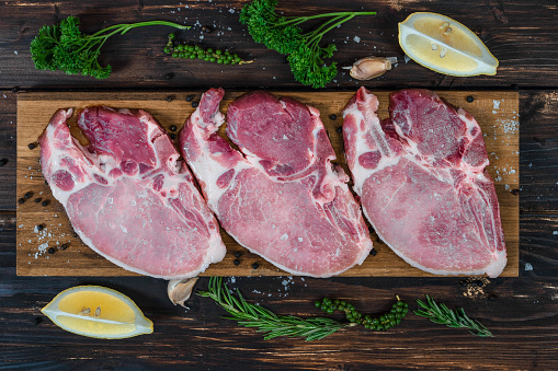 food background of fresh raw meat of pork chop cutlet steak on wooden board with lemon, green pepper, thyme andv black pepper