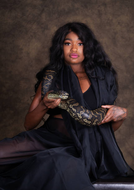 istock Young Black woman holding large boa constrictor, looking at camera. 1211466121