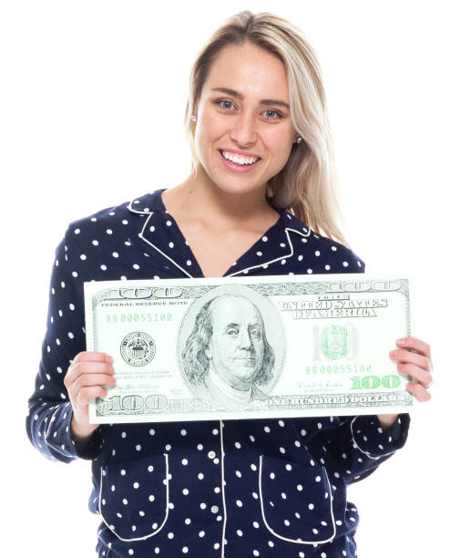 mujer caucásica de pie frente al fondo blanco usando pijama y sosteniendo la moneda - laughing women us paper currency isolated fotografías e imágenes de stock