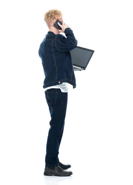 istock Caucasian male standing in front of white background wearing t-shirt and using computer 1211477684