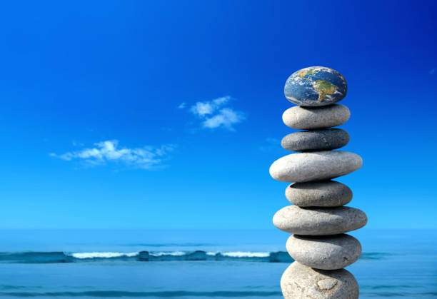 Pile of stones with rock shaped Planet Earths over seascape and clear blue sky. NASA world map image layered and manipulated; https://apod.nasa.gov/apod/image/0304/bluemarble2k_big.jpg