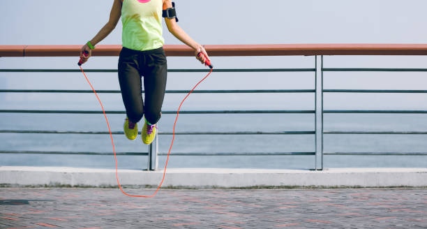 jeune femme de forme physique sautant la corde au bord de mer - jumping women running vitality photos et images de collection