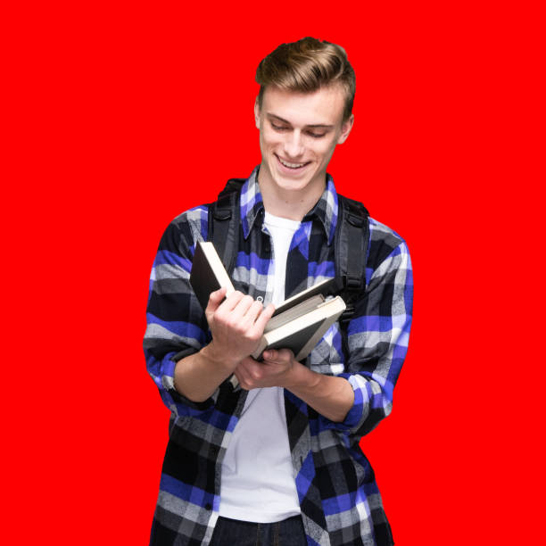 One person of aged 16-17 years old with brown hair caucasian young male university student in front of colored background wearing button down shirt who is studying and holding textbook