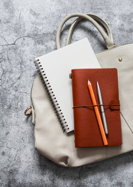 istock Women's business white leather bag with office accessories notepad organizer on a grey background, top view 1211493563