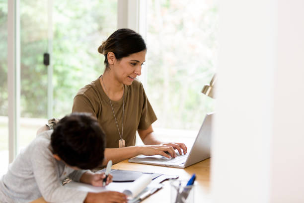 While son draws mother enjoys emailing on her laptop As they both sit at the desk in their living room, the young boy draws and the mother uses her laptop to keep in touch. proud army mom stock pictures, royalty-free photos & images