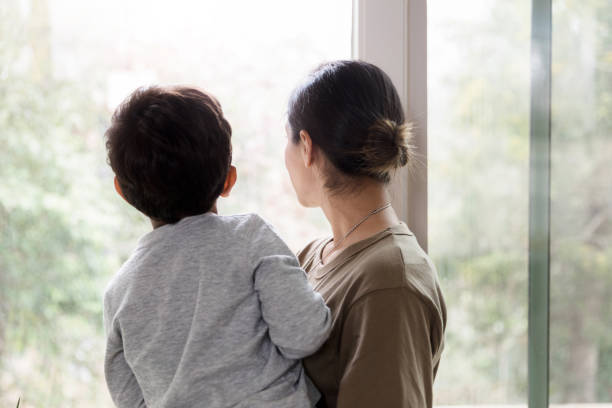 istock Rear view mother and son looking out windows 1211494789