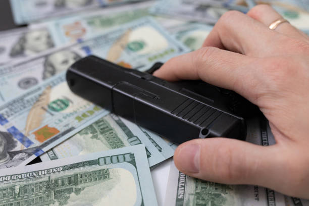 hand holding a gun lies on a pile of money - gun handgun violence kidnapping imagens e fotografias de stock