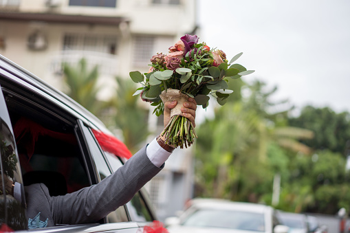 Bridegroom holding flower bouquet out from bridal car