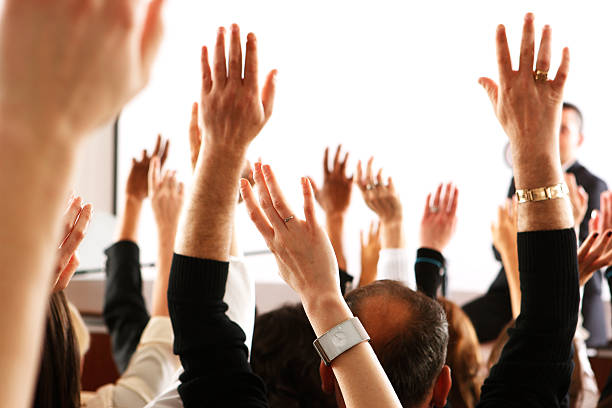 Voting audience, business spectators or students raising hands in seminar Big audience of people raising their hands to vote in favor of some topic. sea of hands stock pictures, royalty-free photos & images