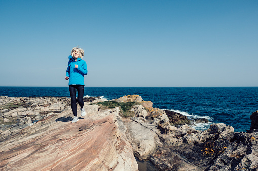 Senior woman jogging on a rocky coastline.