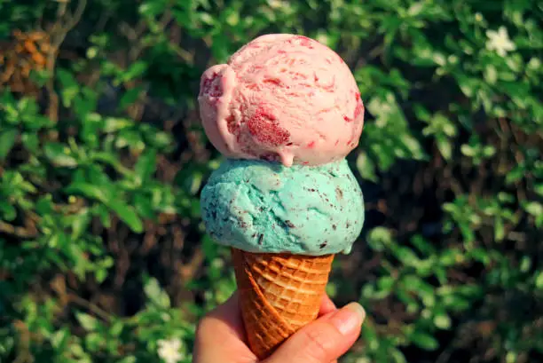 Photo of Hand holding two scoops of ice cream cone melting in the sunlight