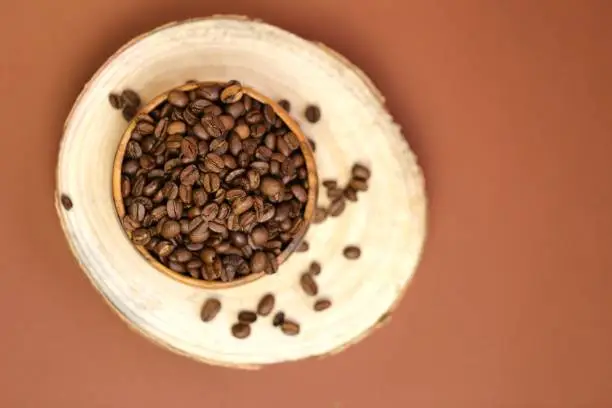 coffee beans in a wooden cup on a cut of a tree on a dark brown background.Coffee drink.Coffee beans in a minimalist style.top view