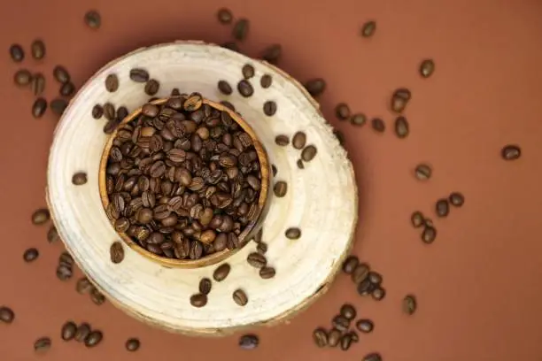 coffee beans in a wooden round cup on a cut of a tree on a dark brown background.Coffee drink.Coffee beans in a minimalist style.top view