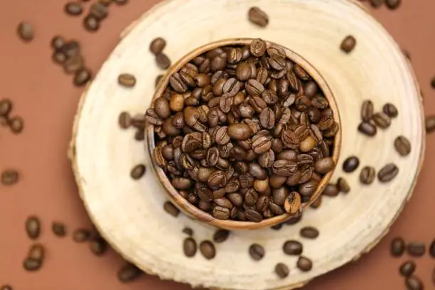 coffee beans in a wooden round cup on a cut of a tree on a brown background.Coffee drink.Coffee beans in a minimalist style.top view