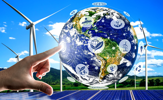 Concept of sustainability development by alternative energy. Man hand take care of planet earth with environmentally friendly wind turbine farm and green renewable energy in background.