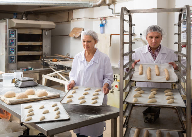 istock Focused baker placing tray with formed raw dough 1211505616