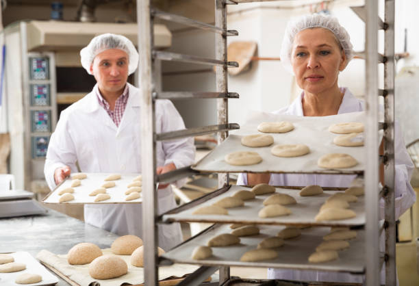 istock Female baker placing tray with formed dough on trolley 1211505623