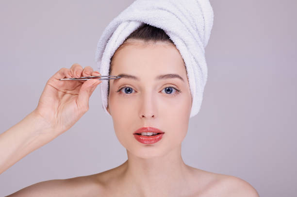 Beautiful young half-naked woman plucking eyebrows with tweezers. stock photo