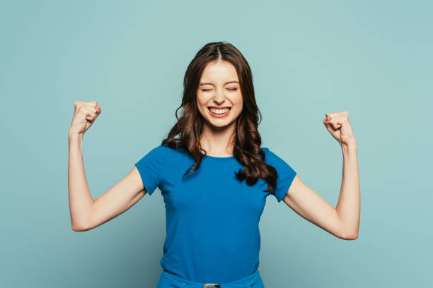 istock excited girl showing winner gesture with closed eyes while smiling on blue background 1211518231