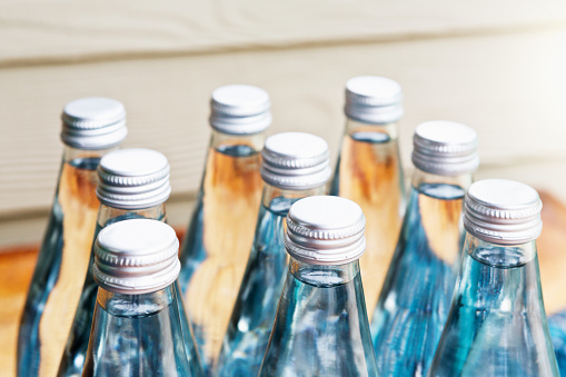 Close up two clear glass bottles of cold lager beer on ice cubes over background of summer sea and sky, low angle side view