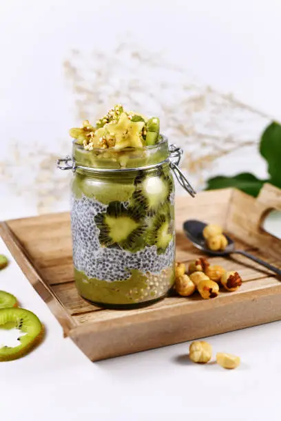 Photo of Green fruit smoothie layered in glass with chia seed pudding topped with star shaped banana and kiwi slices on wooden tray