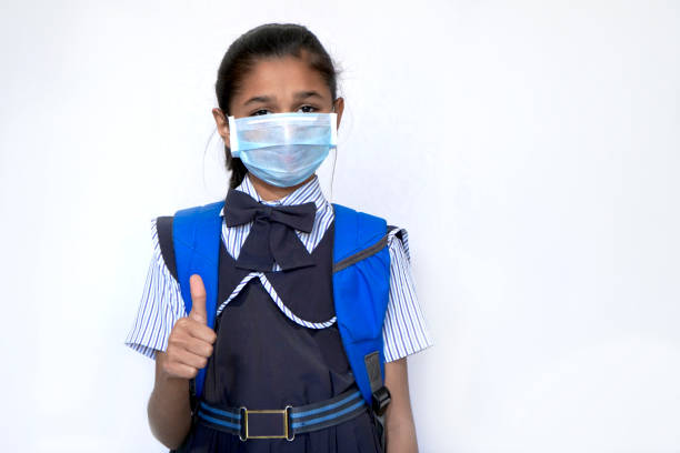 schoolgirl wearing surgical face mask, showing thumps up and looks at camera. - thumps up imagens e fotografias de stock