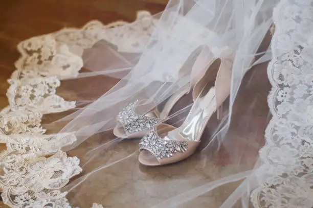 stylish bride's high-heeled shoes, decorated with stones, stand on the floor, next to a white lace veil