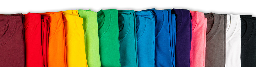 wide panorama row of many fresh new fabric cotton t-shirts in colorful rainbow colors isolated. Pile of various colored shirts on white background
