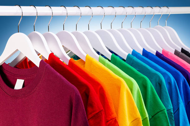 fila di molte nuove t-shirt in cotone in tessuto fresco in colori arcobaleno colorati appesi sul binario dei vestiti in wrdrobe. varie camicie colorate sfondo bianco blu. concetto di moda di stampa fai-da-te. - clothes rack foto e immagini stock