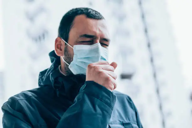 Photo of Young man wear face mask and coughing outdoors.