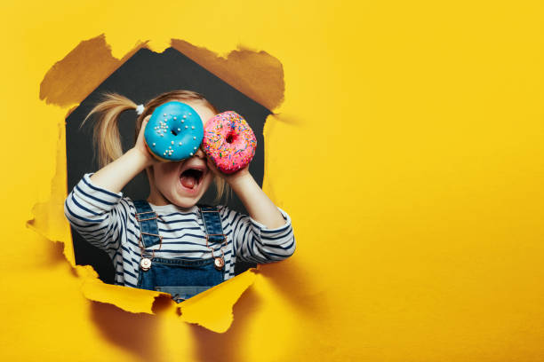 Happy cute boy is having fun played with donuts on black background wall. stock photo