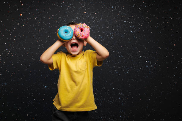 Happy cute boy is having fun played with donuts on black background wall. stock photo