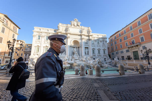 policial usando máscara facial caminha pela deserta praça da fonte trevi, roma, itália - trevi fountain rome fountain monument - fotografias e filmes do acervo