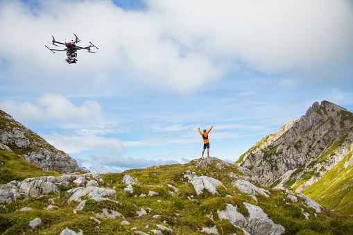 Man celebrating his victory over the mountain. Hands in the air. Drone filming the scene.