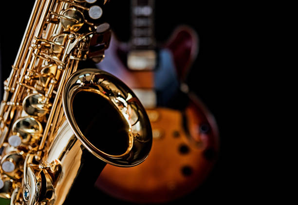 Shiny saxophone and electric guitar against black background A shiny brass sax in the foreground and a dark electric guitar behind, both on a black background. big band jazz stock pictures, royalty-free photos & images