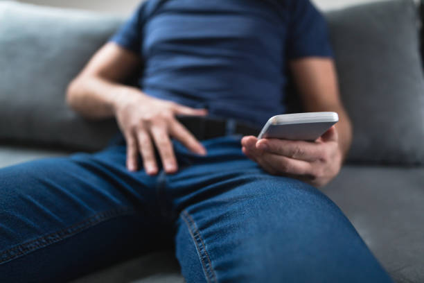 Man holding modern smartphone / cellphone and watching XXX videos on a home couch. Taboo still in modern times. Man holding modern smartphone / cellphone and watching XXX videos on a home couch. Taboo still in modern times. penis photos stock pictures, royalty-free photos & images