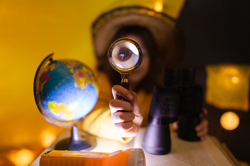 Young female child using magnifying glass to explore earth globe in a home made livingroom tent with light balls.